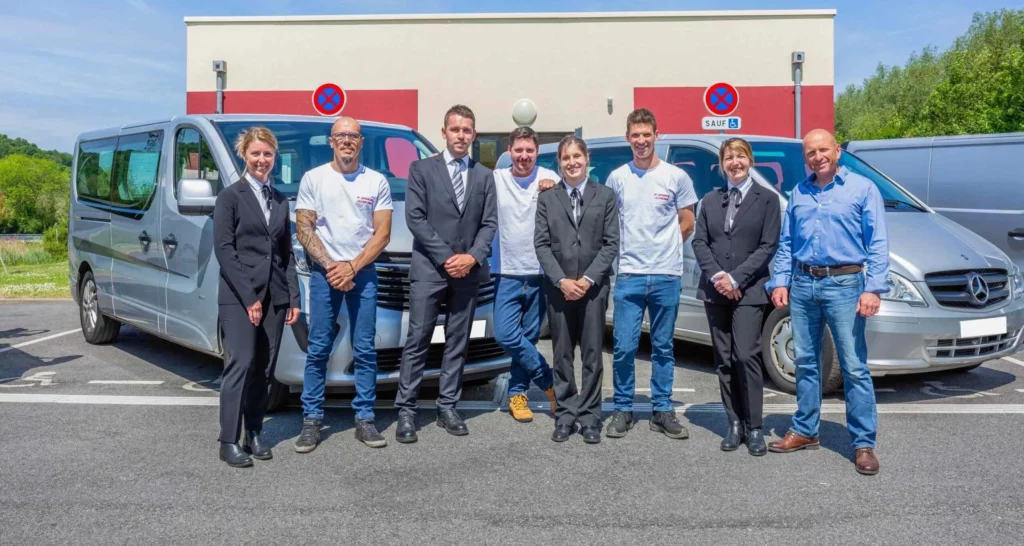 Équipe au complet des pompes funèbres et marbrerie posant devant les véhicules professionnels