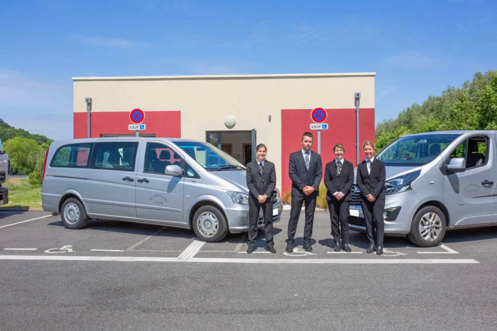 Conseillers funéraires en costume sombre posant devant deux corbillards et la maison funéraire