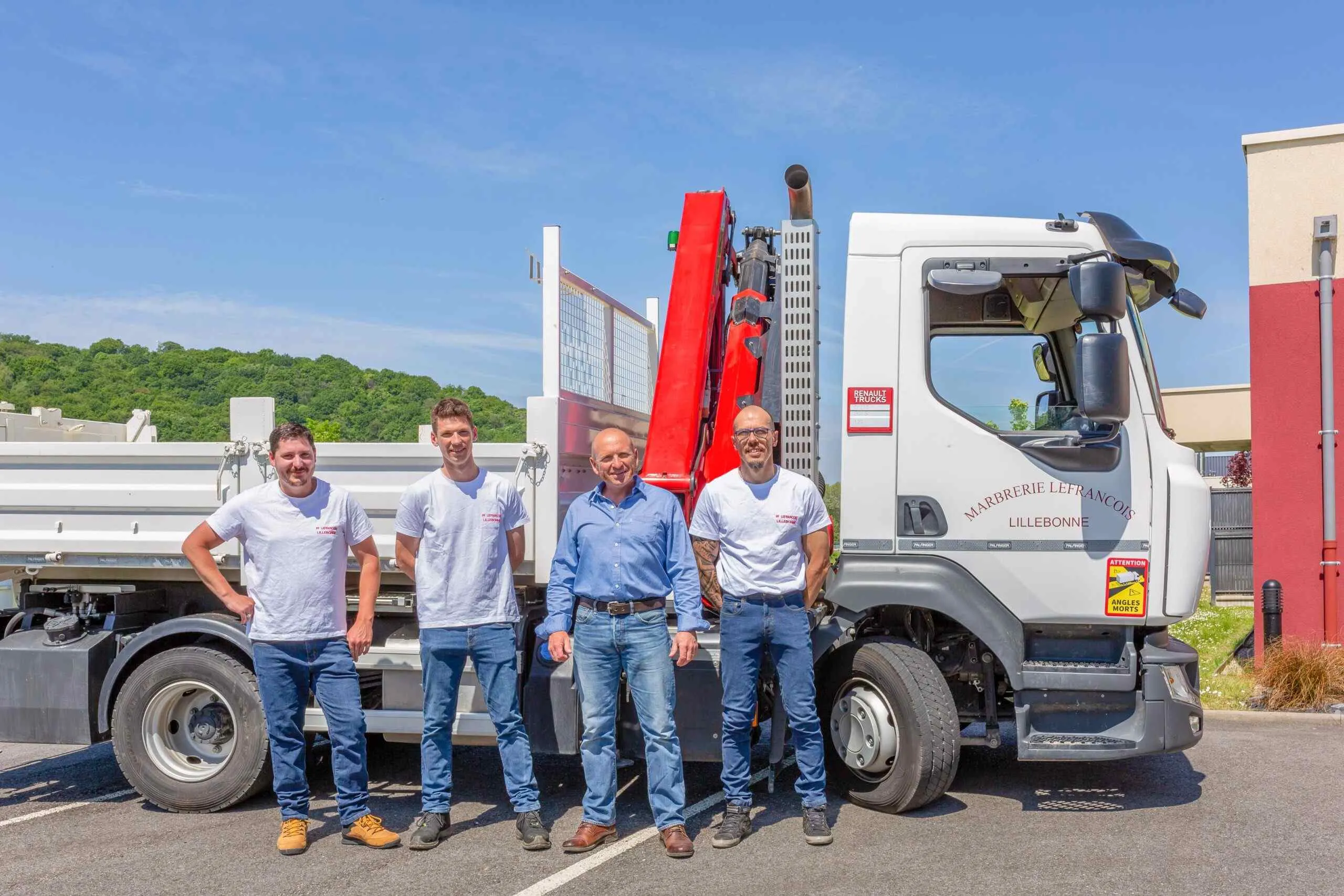 Équipe de marbrerie funéraire posant devant un camion de transport équipé d'une grue