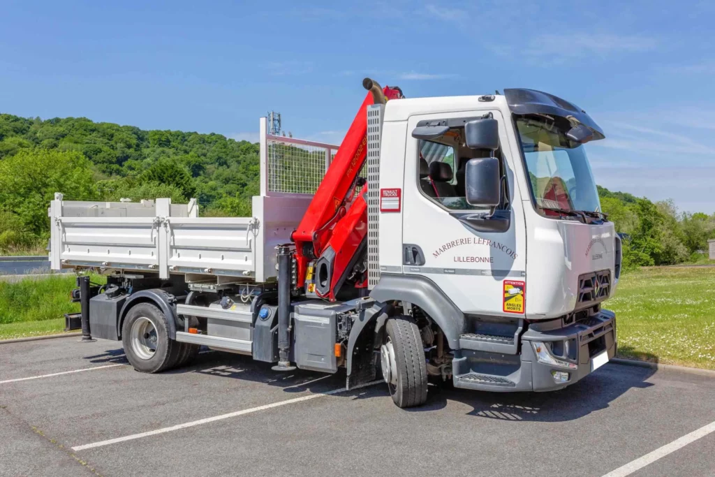 Camion de marbrerie funéraire blanc équipé d'une grue hydraulique rouge stationné en extérieur