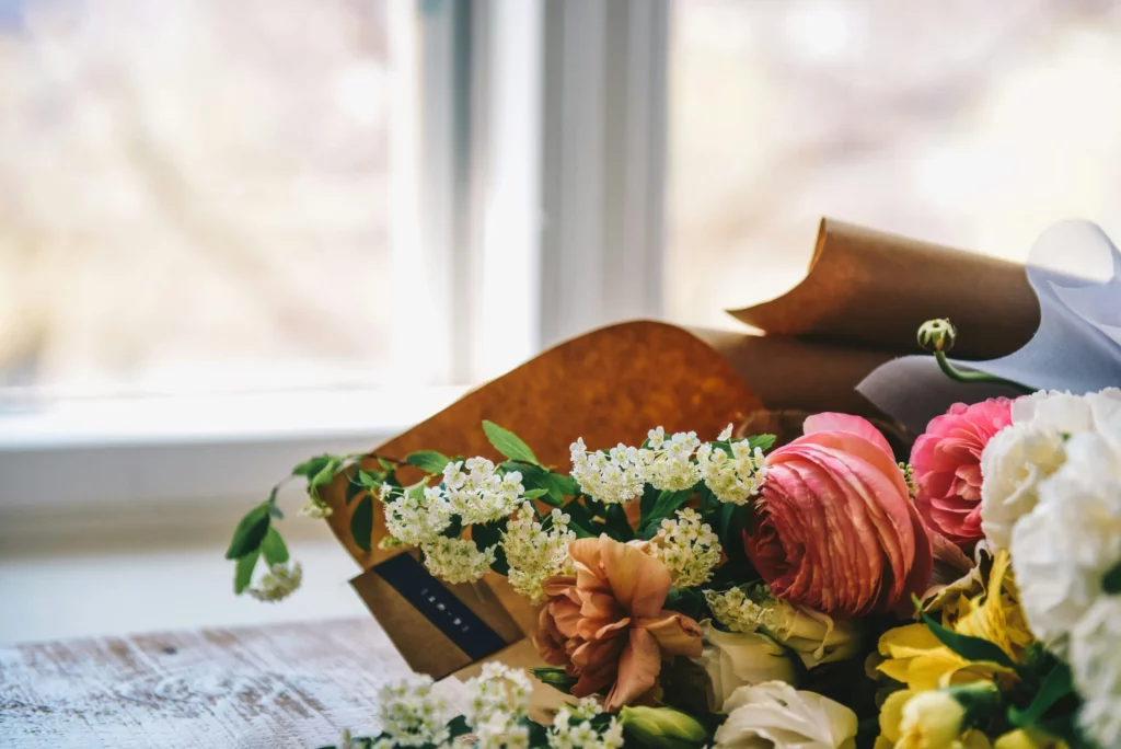 Bouquet de fleurs fraîches et délicates enveloppé dans du papier kraft posé près d'une fenêtre